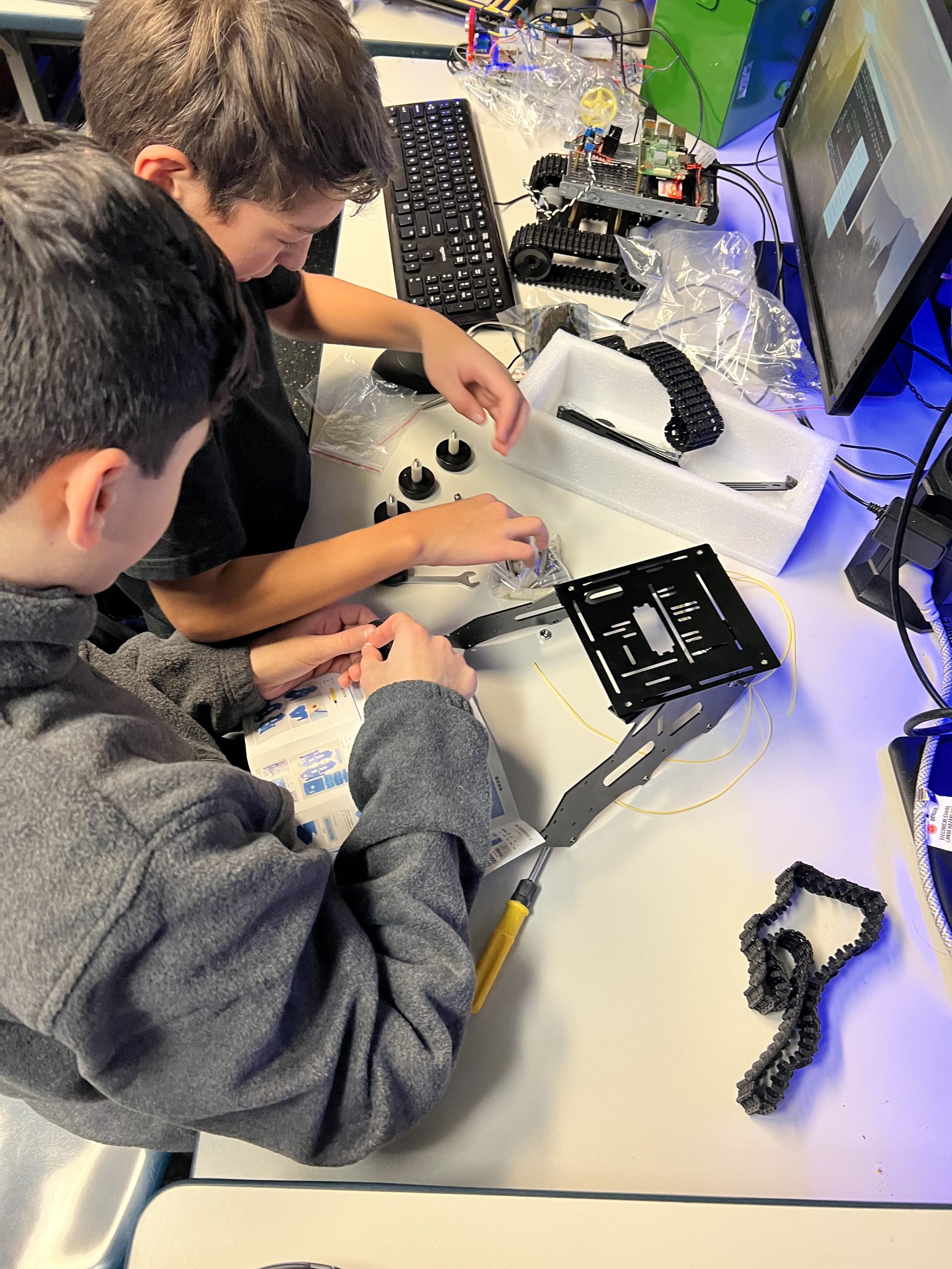 Two students assembling tracked robot chassis with tools at Plum Crazy Robotics class Marlboro NJ