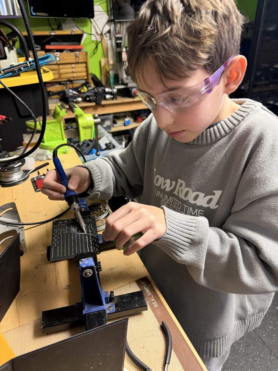 Student soldering circuit board with safety goggles at Plum Crazy Robotics electronics workbench Marlboro NJ