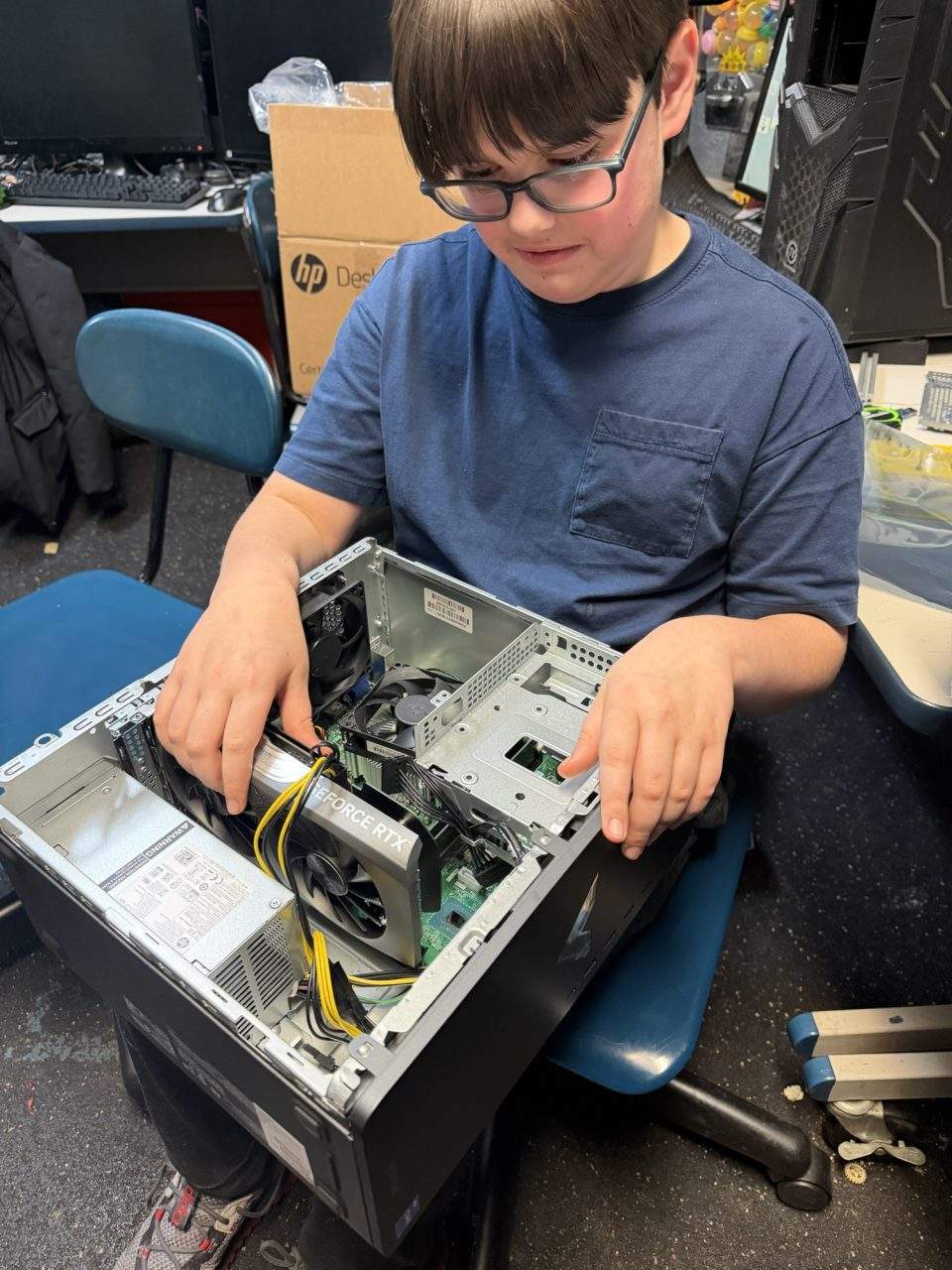 Student examining motherboard and GeForce RTX GPU inside open computer case at Plum Crazy Robotics