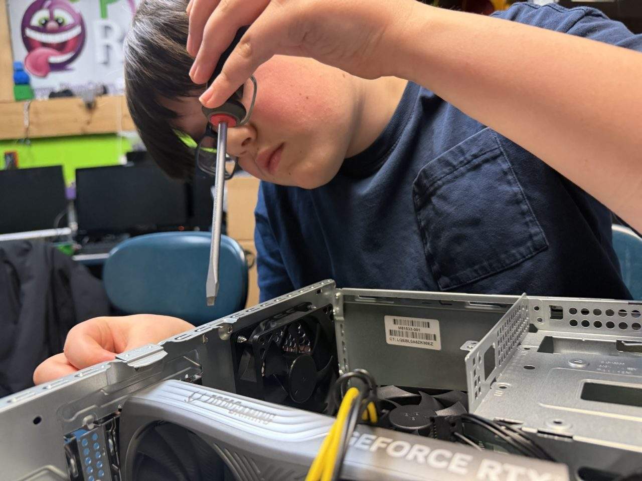 Student using screwdriver to secure components inside desktop PC at Plum Crazy Robotics electronics class