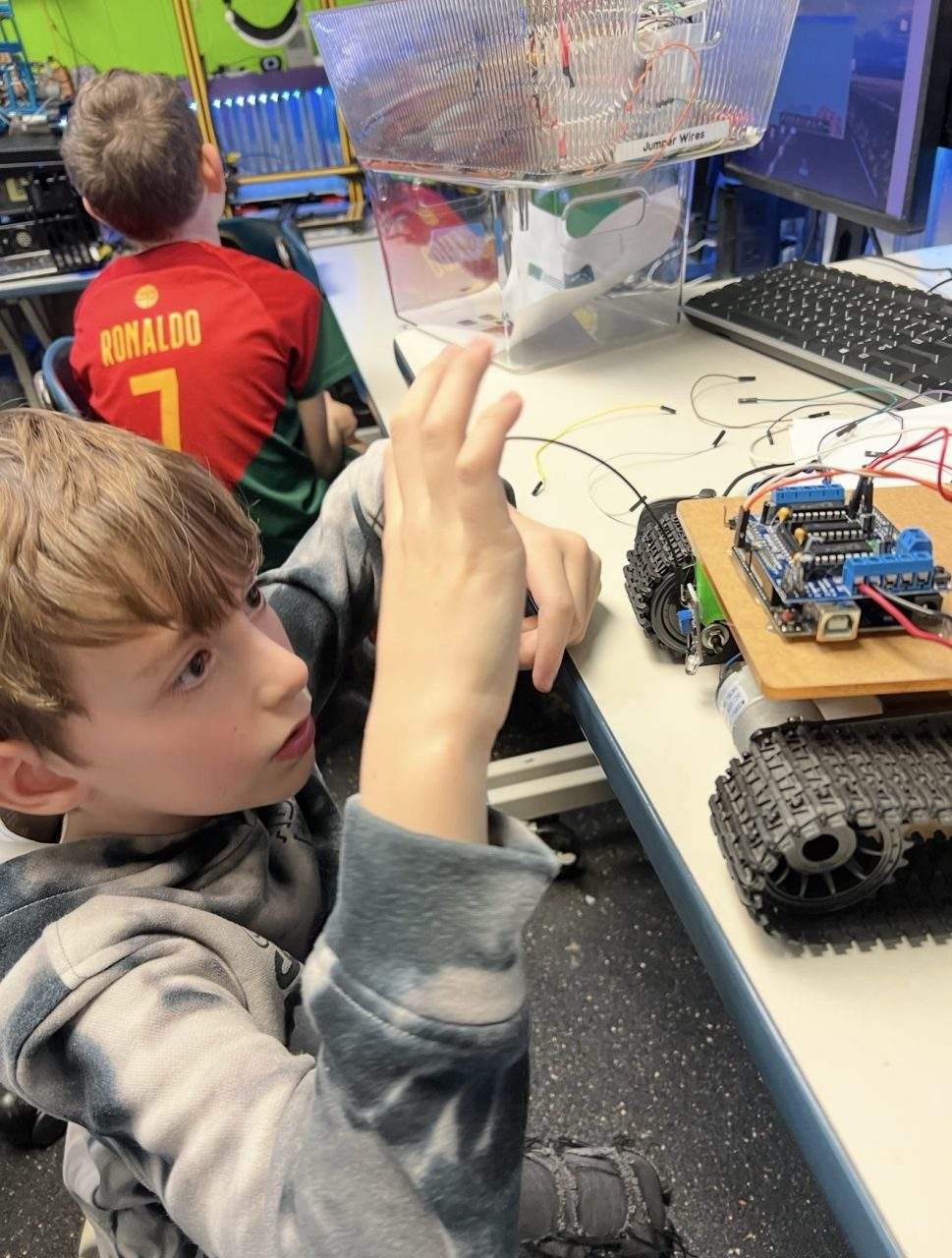 Student with Arduino tracked robot and clear plastic housing at Plum Crazy Robotics class Marlboro NJ