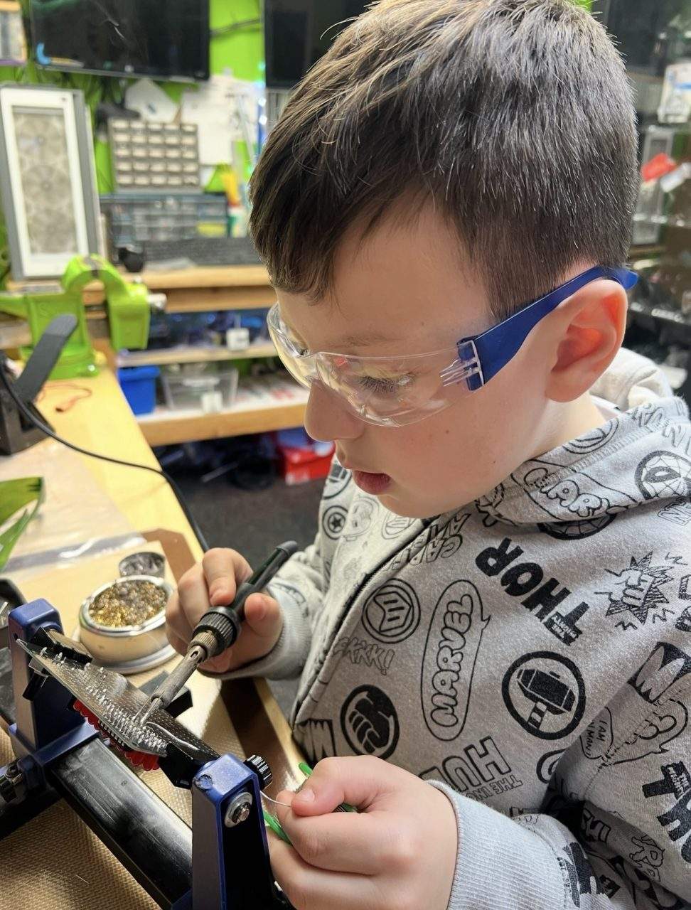 Young student soldering with safety goggles at electronics workstation at Plum Crazy Robotics Marlboro NJ