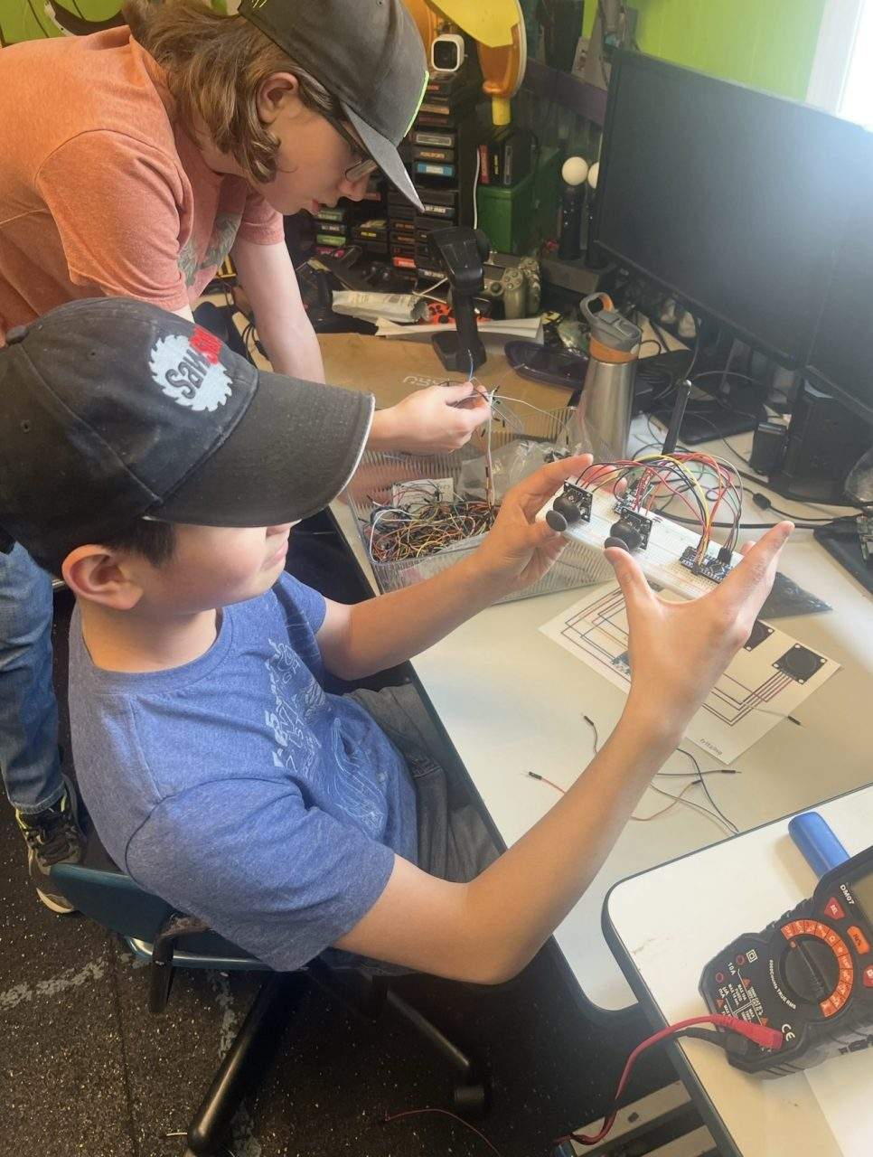 Two students wiring breadboard circuit with multimeter and Arduino motor driver at Plum Crazy Robotics combat robotics class NJ